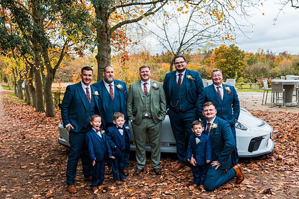 Groomsmen in autumn forest, wearing matching suits, smiling.