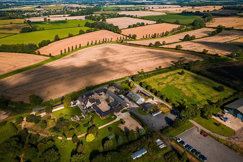 Aerial view of a countryside landscape with farms, fields, trees, and buildings under a partly cloudy sky. Image by Documentary Wedding Photographer Lewis Bishop Photography.