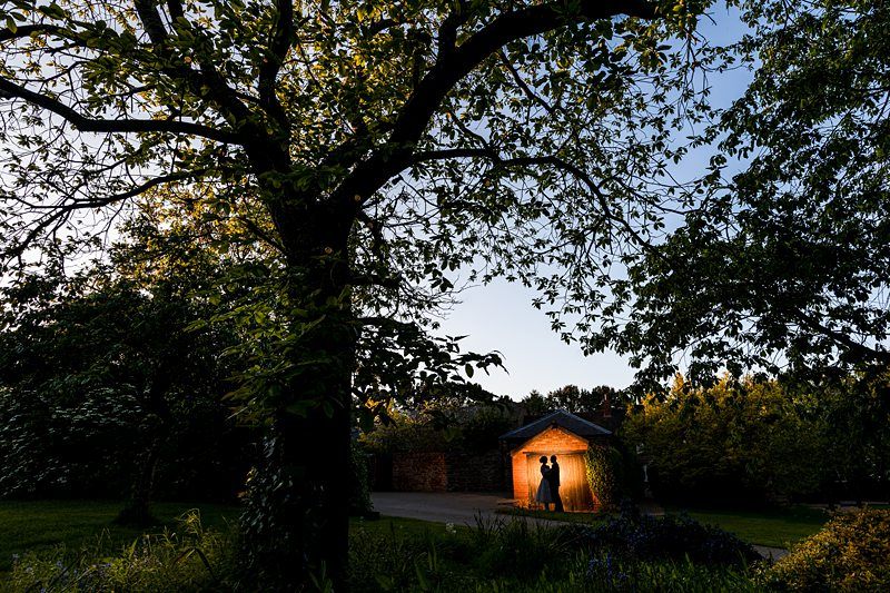 Two people share a dance inside a lit gazebo in a dark, tree-filled garden at dusk. Image by Documentary Wedding Photographer Lewis Bishop Photography.