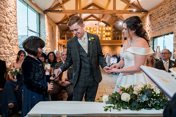 Couple exchanging rings at rustic wedding ceremony.