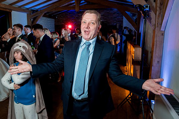 Man dancing at party with child in background.