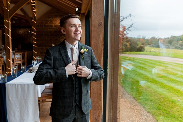 Groom in suit smiling beside window at countryside venue.