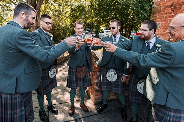 Men in kilts toasting at outdoor event.
