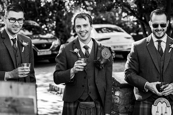Three men in kilts smiling at wedding.