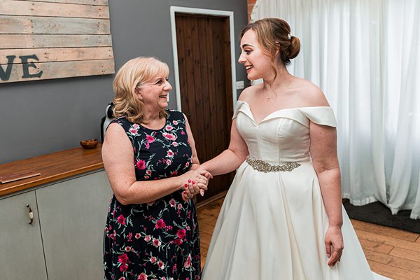 Bride and older woman smiling and shaking hands.