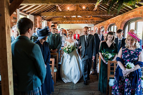 Bride walking aisle in rustic wedding venue.