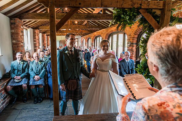 Bride and groom smiling at wedding aisle in rustic venue.