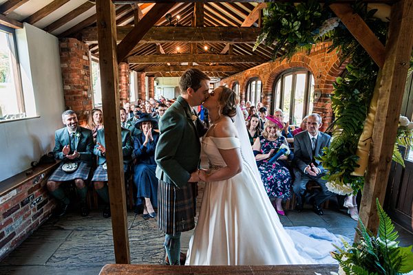 Bride and groom kissing at rustic wedding ceremony.