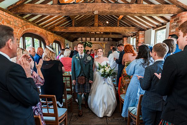 Bride and groom walking down aisle post-ceremony, guests applauding.