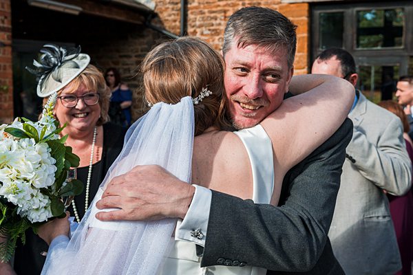 Bride embracing man at sunny outdoor wedding reception.