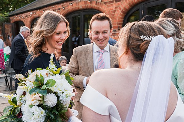 Wedding guests greeting bride with flowers outdoors.