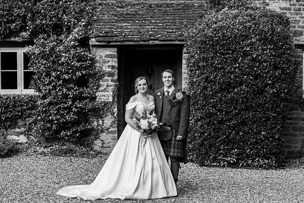 Couple in wedding attire outside brick building.