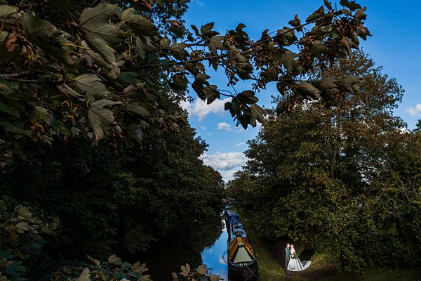 Canal with moored boats and overhanging trees in countryside.