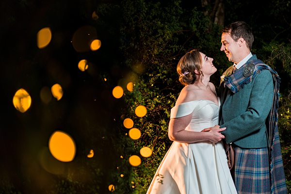 Couple in wedding attire with fairy lights at night.