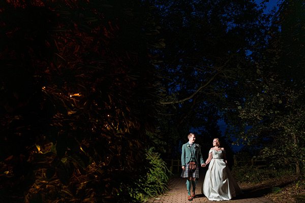 Couple in wedding attire walking at night under trees.