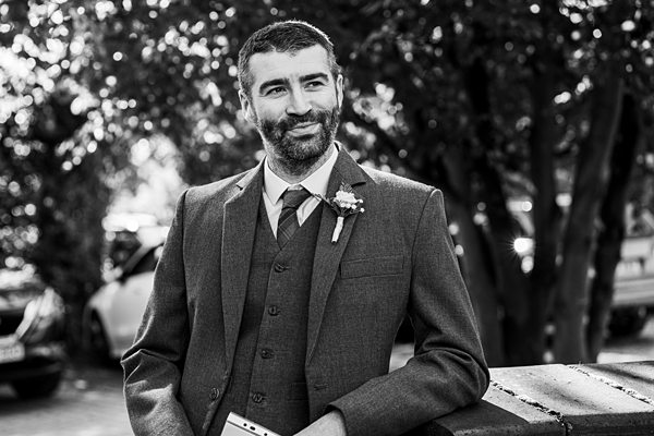 Groom in suit smiling outdoors, black and white photo.