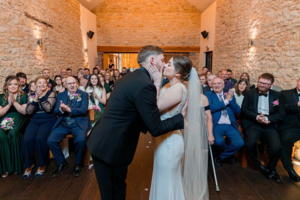Bride and groom kissing at wedding ceremony with guests.