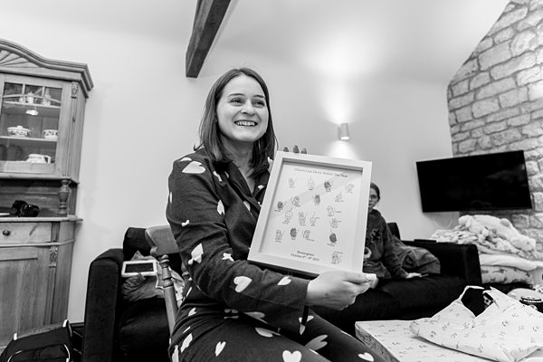 Woman smiling, holding framed artwork, cozy indoor setting.