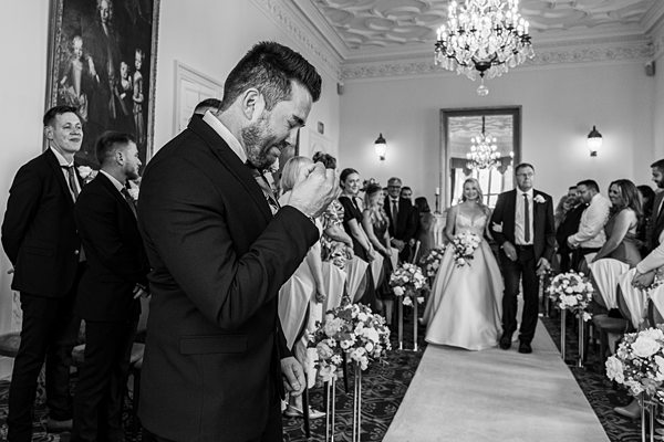 Emotional groom watching bride walk down the aisle.