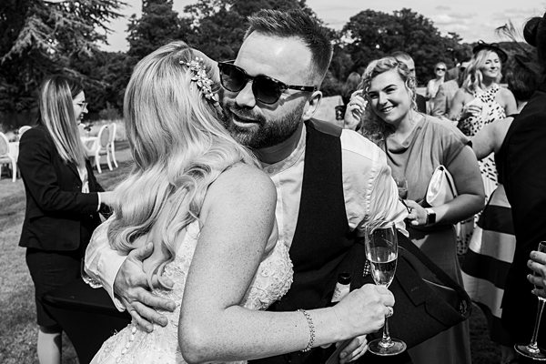 Bride and groom embracing at wedding reception, guests watching.