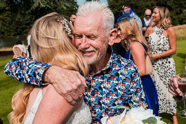 Wedding hug, joyful father, bride, guests background.
