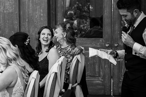 Guests laughing at wedding, speaker with microphone.