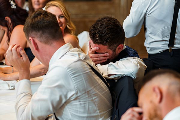 Man emotionally embracing friend at wedding reception.