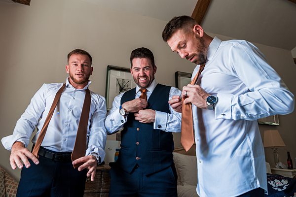 Three men adjusting ties and smiling in a room.