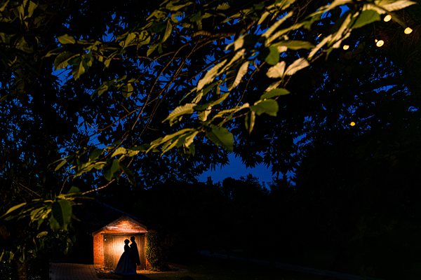Couple under tree at dusk, lit gazebo behind.