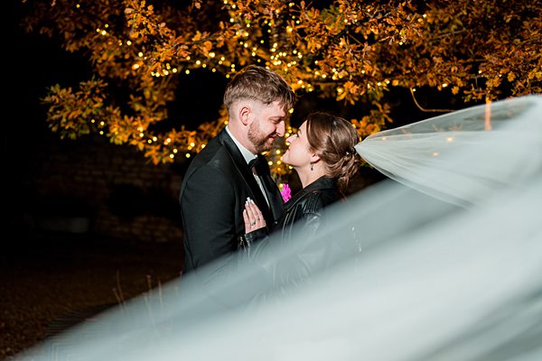 Couple embracing at night under illuminated tree.