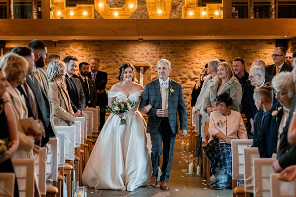 Bride walking down aisle with father, wedding ceremony.