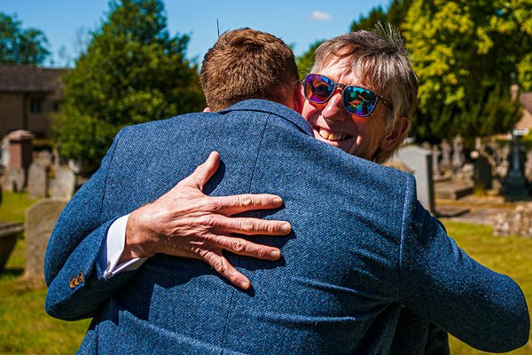 Embracing people smiling outdoors on a sunny day.