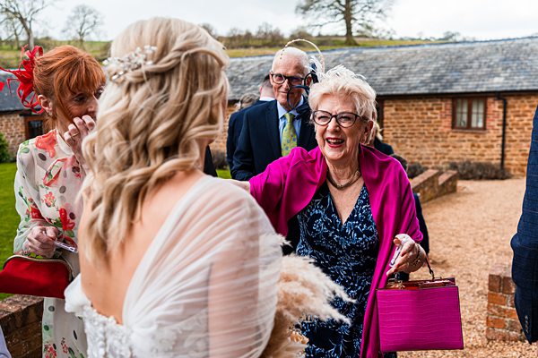 Joyful wedding guests greeting bride outdoors.