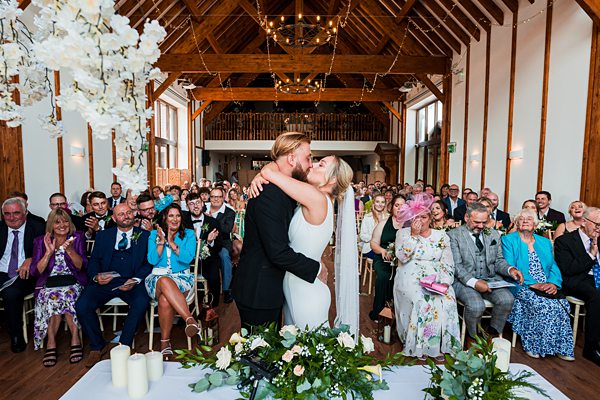 Bride and groom kissing at wedding ceremony in barn venue.