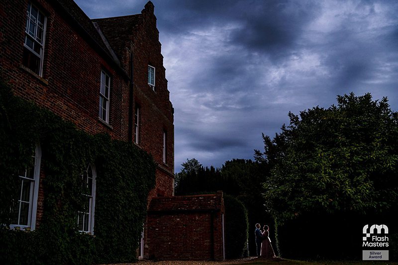 Couple embracing by historic brick building at dusk.
