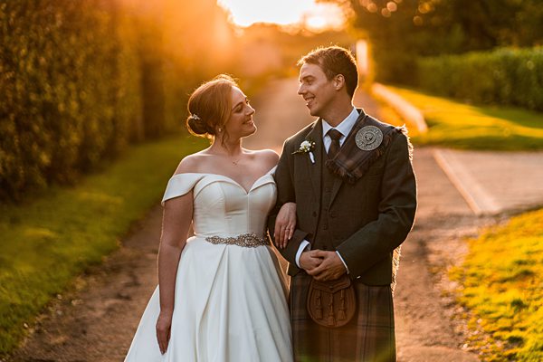 Bride and groom in sunset light, wedding attire.