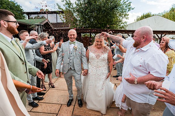 Wedding guests tossing confetti at smiling bride and groom.