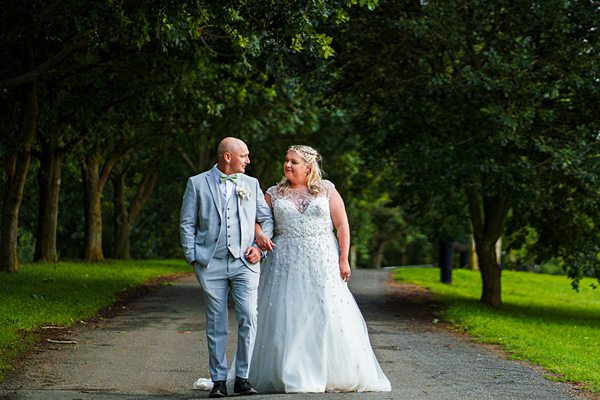 Couple in wedding attire walking in park.