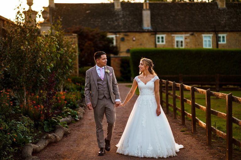 Couple walking in garden at sunset, wedding attire.