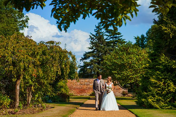 Couple walking in garden on sunny wedding day.