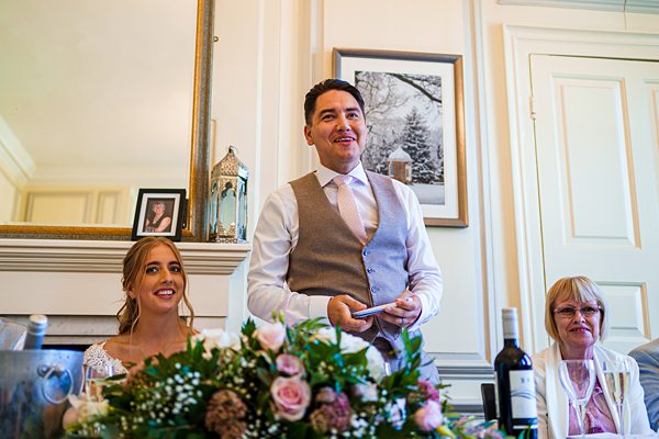 Man giving speech at wedding reception, guests smiling.