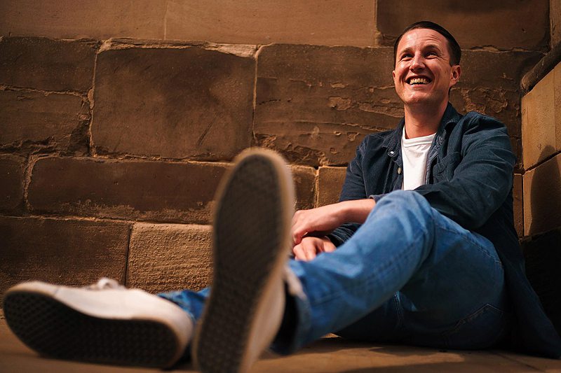 Man sitting and laughing against brick wall.