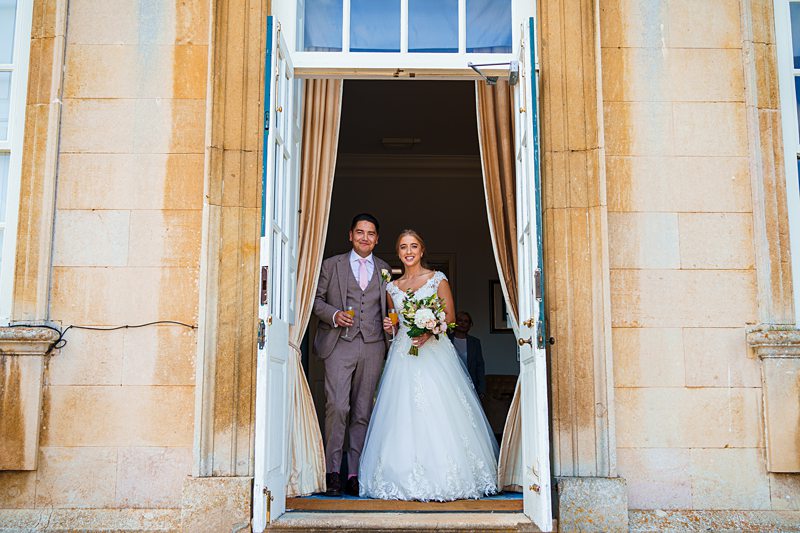 Bride and groom at manor entrance with bouquet.