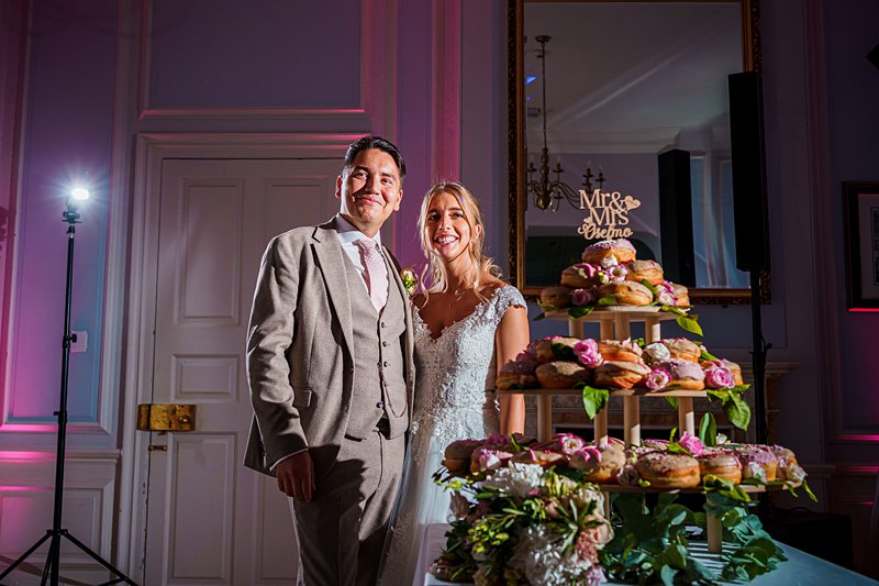 Bride and groom posing with wedding cake in elegant venue.