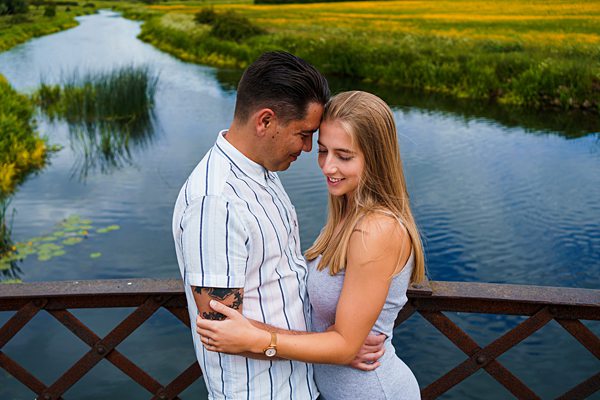 Couple embracing on bridge over river.