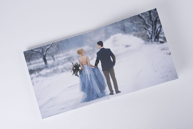 Couple in winter wedding attire walking on snowy path.