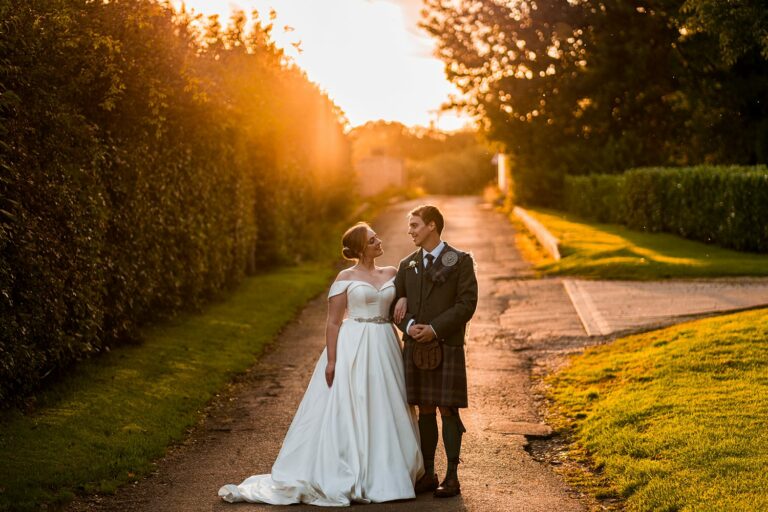 Couple in wedding attire smiling at sunset.