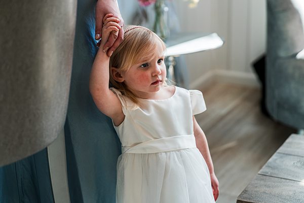 Child in white dress standing pensively indoors.