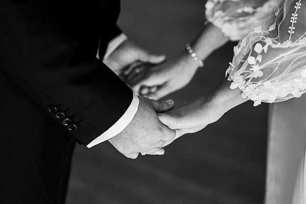 Couple holding hands in wedding attire, black and white photo.