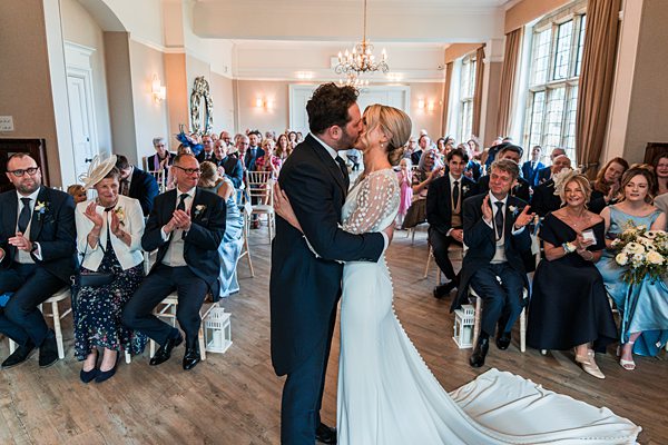 Bride and groom kissing at wedding ceremony with guests.